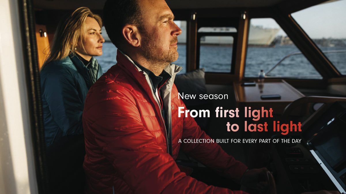 A man in a red puffer jacket and a woman in a blue jacket sitting inside a boat cabin, with overlaid text reading 'New season From first light to last light' and 'A COLLECTION BUILT FOR EVERY PART OF THE DAY'.