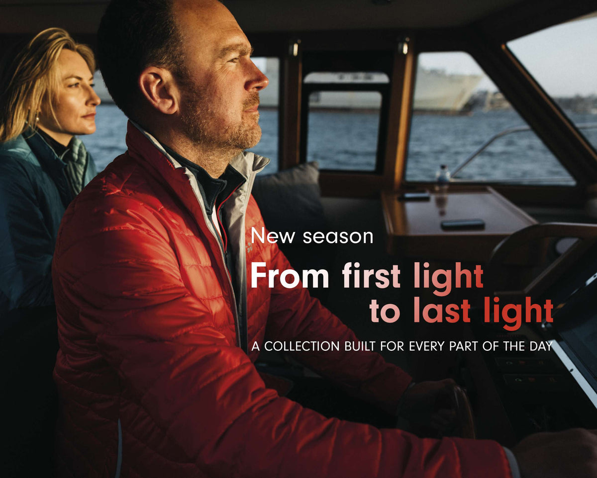 A man in a red puffer jacket driving a boat while a woman sits beside him. Large overlaid text reads 'New season From first light to last light' and 'A COLLECTION BUILT FOR EVERY PART OF THE DAY.