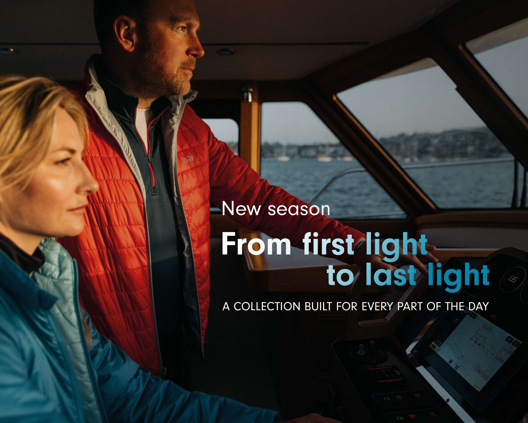 A man and a woman inside a boat cabin at dusk, wearing outdoor jackets. Large overlaid text reads 'New season From first light to last light A COLLECTION BUILT FOR EVERY PART OF THE DAY.